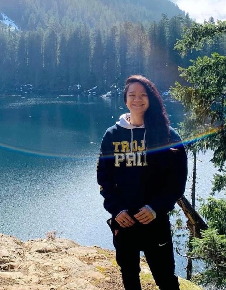 Ari smiling beside a lake with forested hills behind her