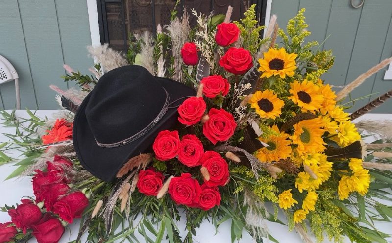 Black cowboy hat surrounded by red roses and sunflowers