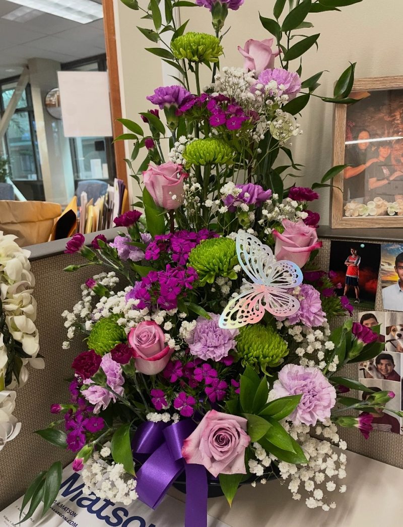 Pink and purple flower arrangement with a purple ribbon and butterfly accents