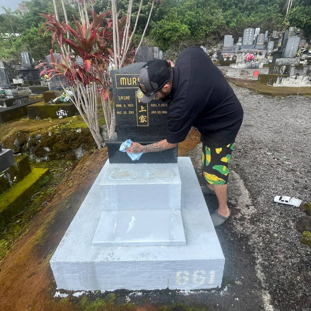 Team member cleaning a concrete memorial base at a Hilo cemetery
